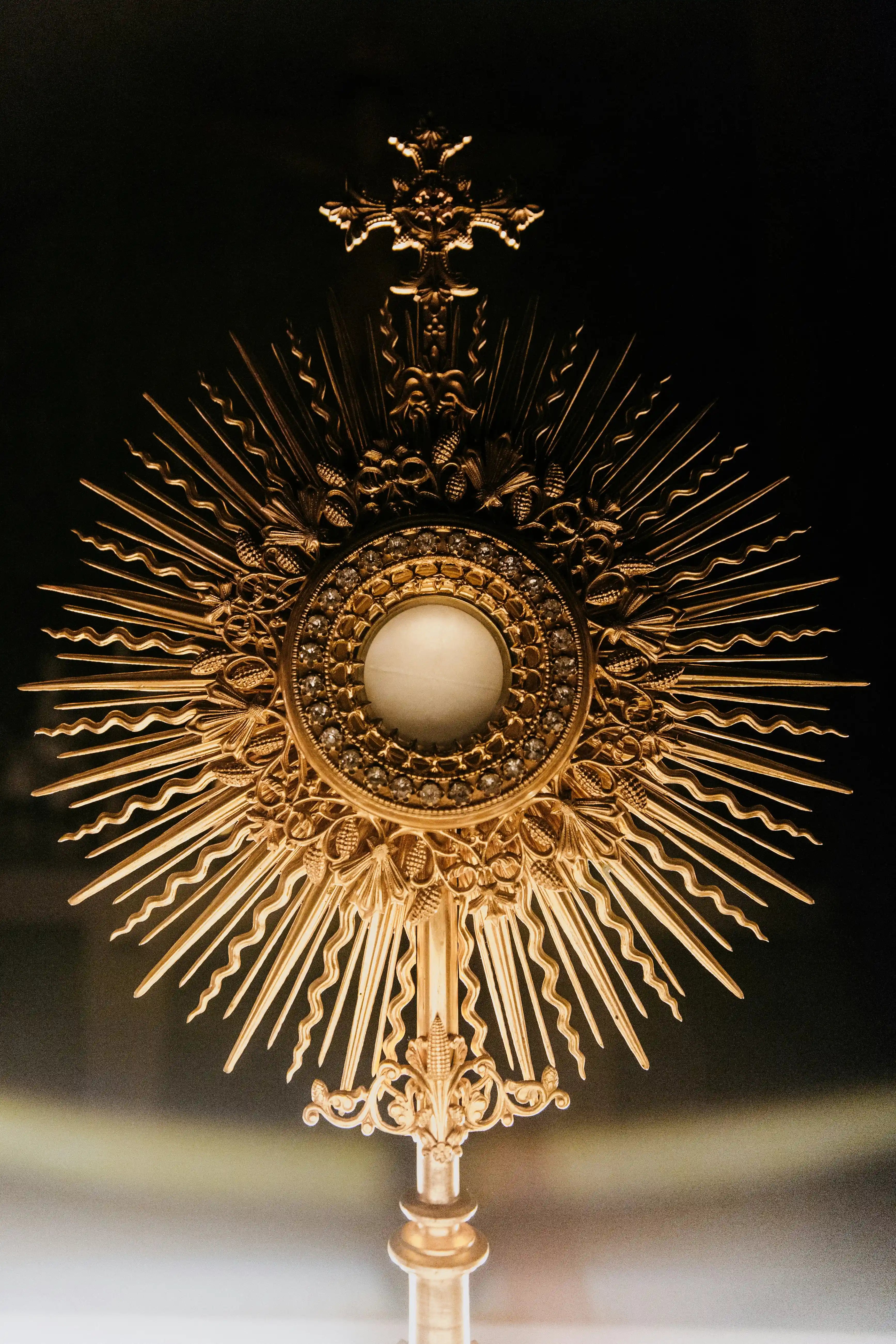 Ornate gold monstrance for Eucharistic Adoration featuring intricate wheat and vine motifs.